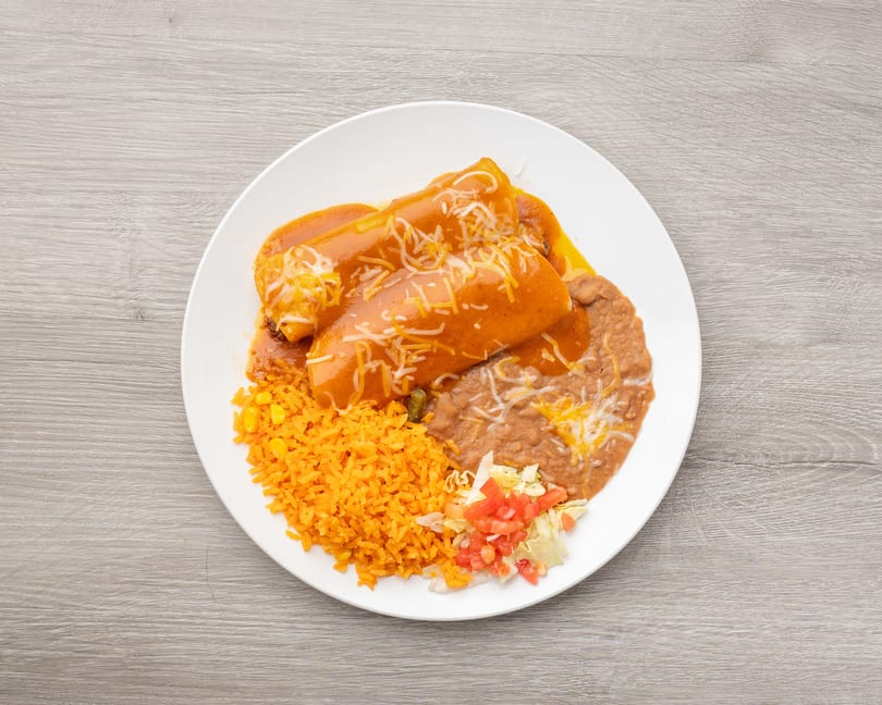 Two enchiladas covered in red sauce and cheese, with rice, refried beans, and a small salad.