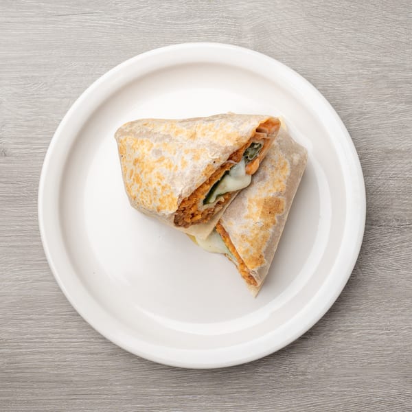 Two halves of a burrito, filled with orange rice, green vegetables, and melted cheese, on a white plate.