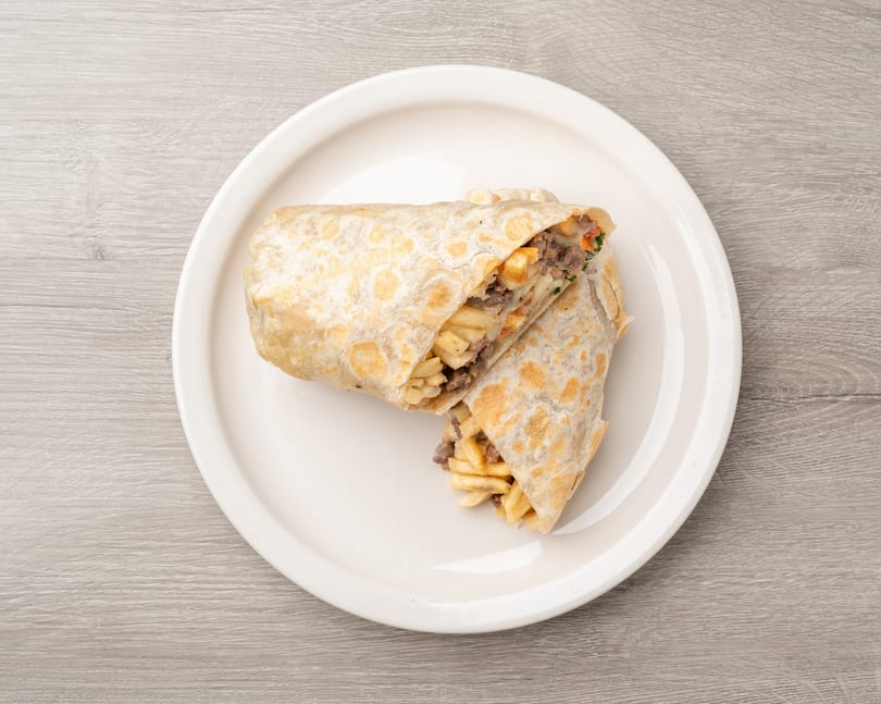 Two halves of a burrito filled with meat, fries, and vegetables on a white plate.
