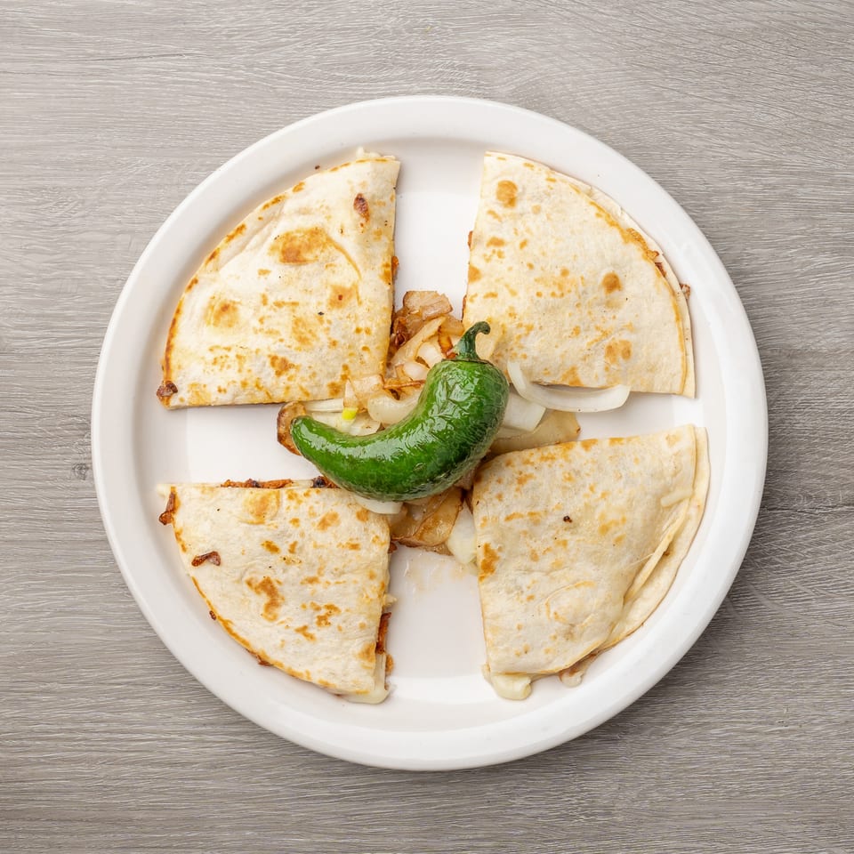 Four quesadilla wedges with melted cheese, grilled onions, and a green chili pepper on a white plate.