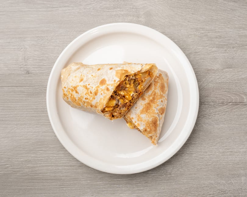 A large breakfast burrito, cut in half to show the filling, on a white plate.