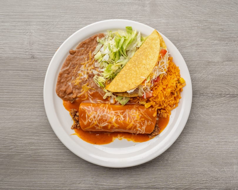 A Mexican combination plate with a burrito, taco, refried beans, rice, and shredded lettuce.